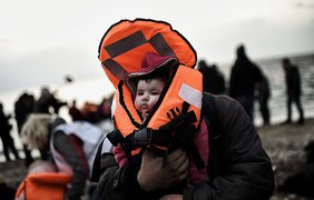 Беженец с ребёнком на руках прибывает на греческий остров Лесбос, переплыв через Эгейское море из Турции