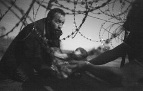 Снимок австралийского фотографа Уоррена Ричардсона, занявший призовое место на фотоконкурсе World Press Photo of the Year. Беженец передаёт ребёнка через забор на сербско-венгерской границе, 28 августа 2015 года
