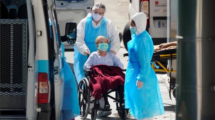 Работники скорой помощи толкают инвалидную коляску с пациентом в доме престарелых недалеко от Мадрида/REUTERS
