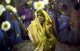 Вдова бросает в воздух цветы во время празднования Холи в ашраме для вдов во Вриндаване, Индия, 14 марта 2014 года.