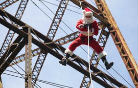 Пожарный в костюме Санта Клауса спускается с моста, чтобы вручить подарки живущим под ним детям, в городе Гватемала, 21 декабря 2014 года.
